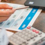 Dłoń przeglądająca dokumenty finansowe przy kalkulatorze i laptopie