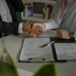 Uścisk dłoni nad podpisanymi dokumentami przy biurku – kancelaria IT